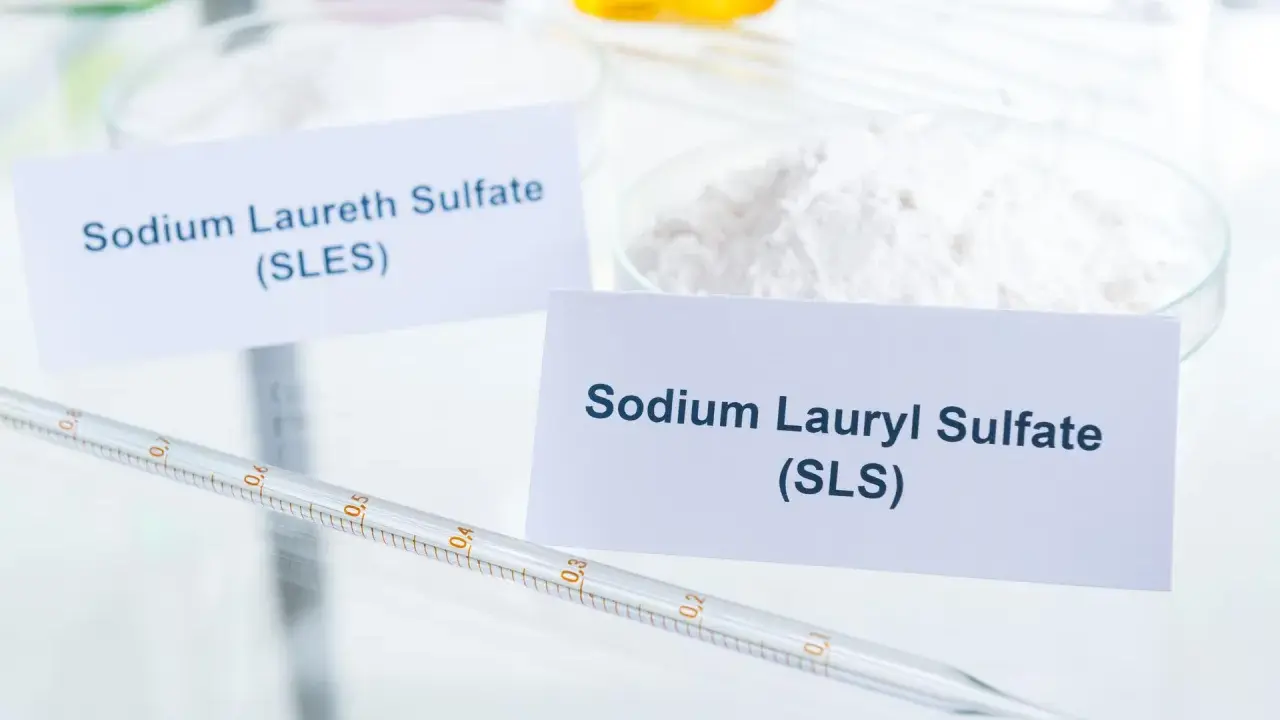 Białe proszki w naczyniach laboratoryjnych, jeden z etykietą "Sodium Laureth Sulfate (SLES)", obok pipeta.
