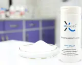 Biały proszek w szalce Petriego i butelka z napisem "Benzoesan benzylu 25%". Produkt do pielęgnacji skóry wrażliwej.