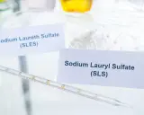 Białe proszki w naczyniach laboratoryjnych, jeden z etykietą "Sodium Laureth Sulfate (SLES)", obok pipeta.