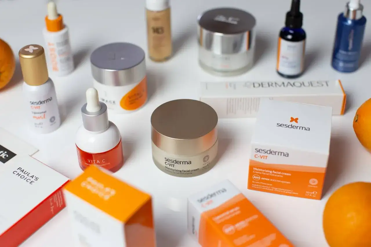 Kremy i serum z witaminą C, w tym Sesderma C-VIT, na białym tle z pomarańczami.